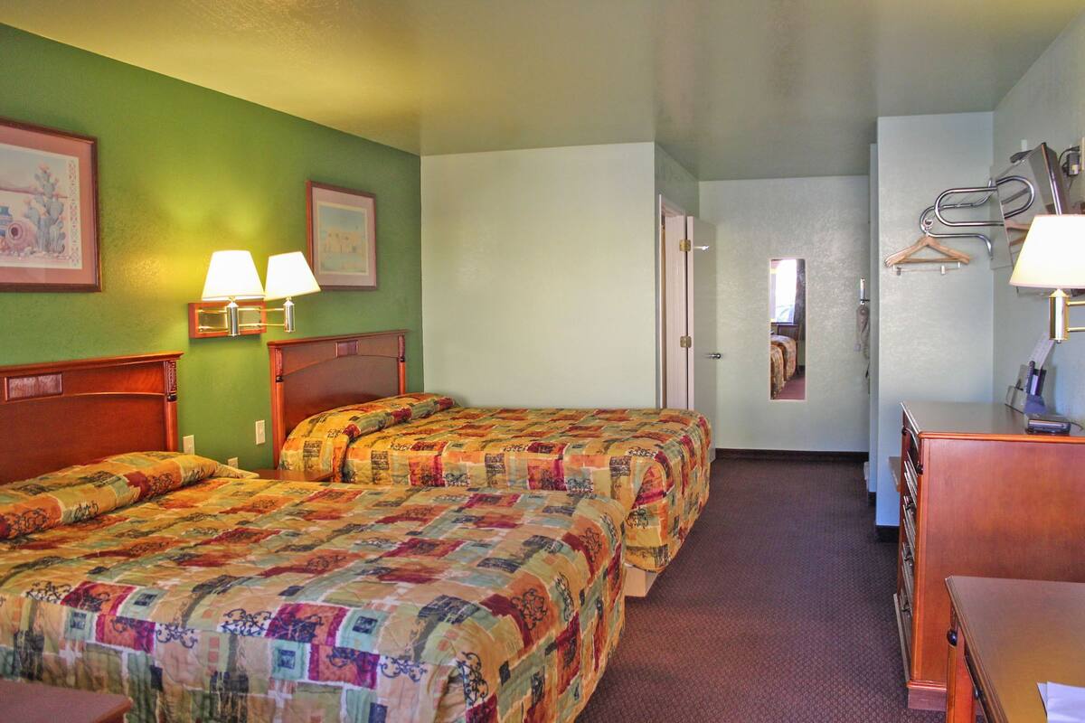 Une chambre d’hôtel avec deux lits, un bureau, une chaise, un miroir et une porte donnant sur une autre pièce.