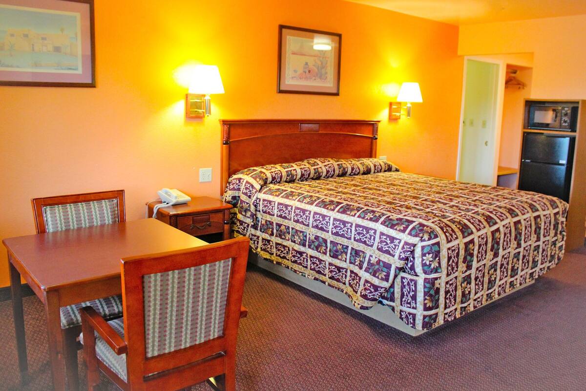 Une chambre d’hôtel équipée d’un lit, d’un bureau, d’une chaise, d’une table de chevet, d’une lampe et d’un réfrigérateur.