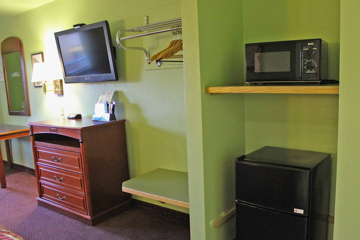 Une chambre d’hôtel équipée d’une commode en bois, d’une télévision, d’un four à micro-ondes et d’un réfrigérateur.