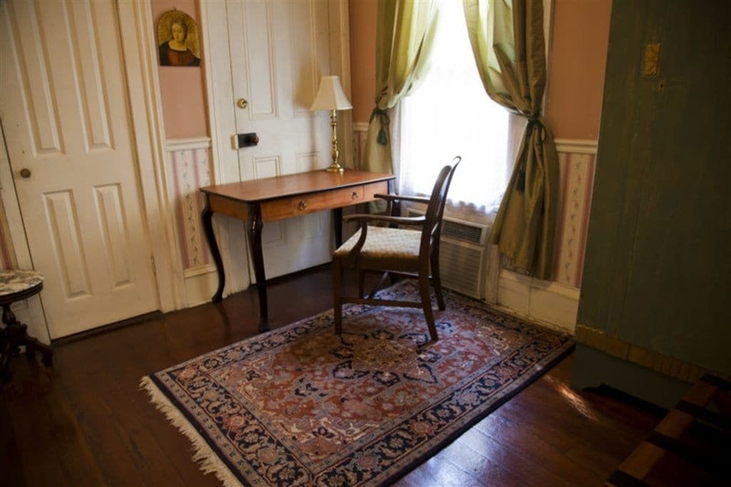 A room with a wooden desk, a chair, a patterned rug, a lamp, and a window with curtains.