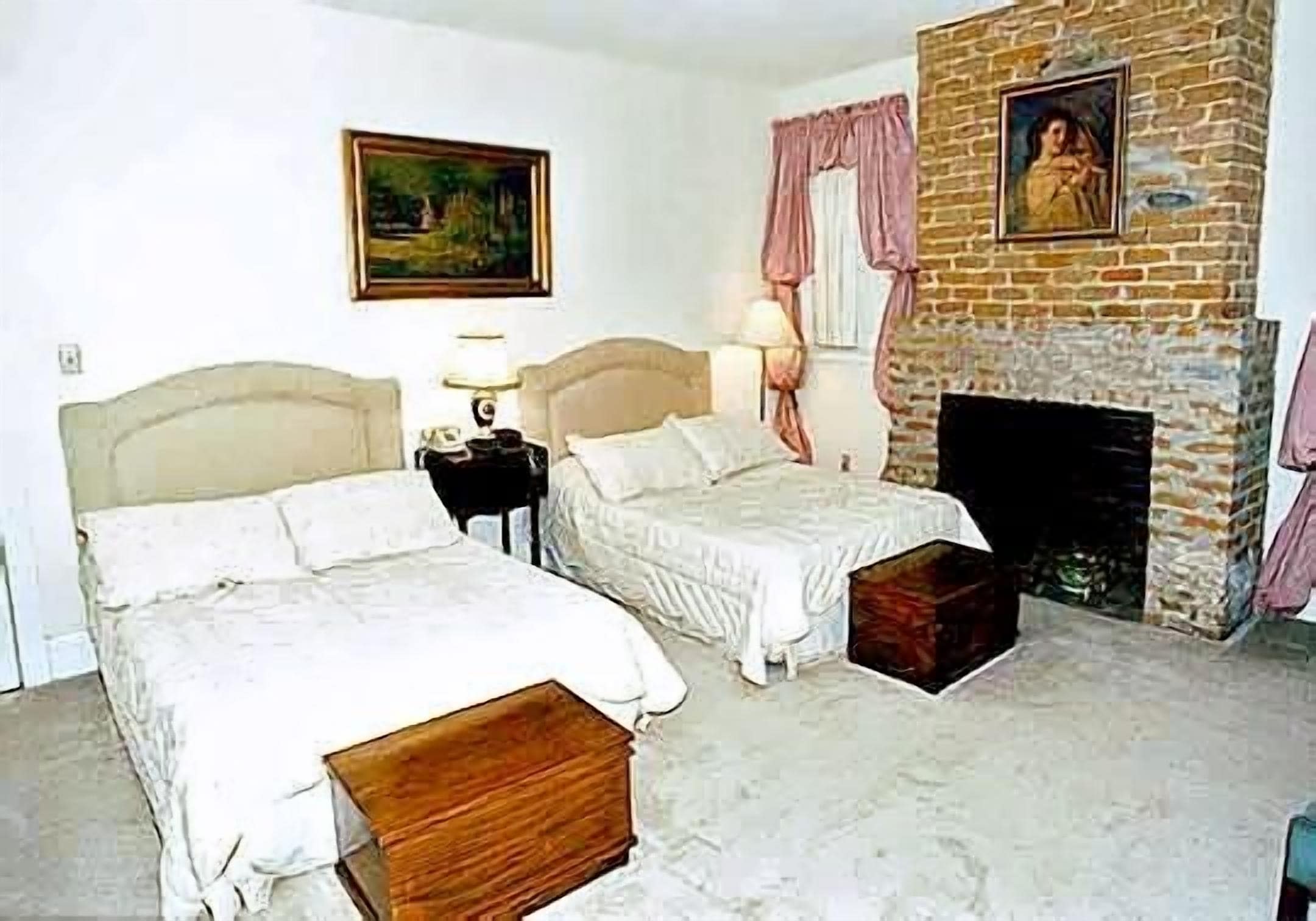 A bedroom with two beds, a fireplace, and a painting on the wall.
