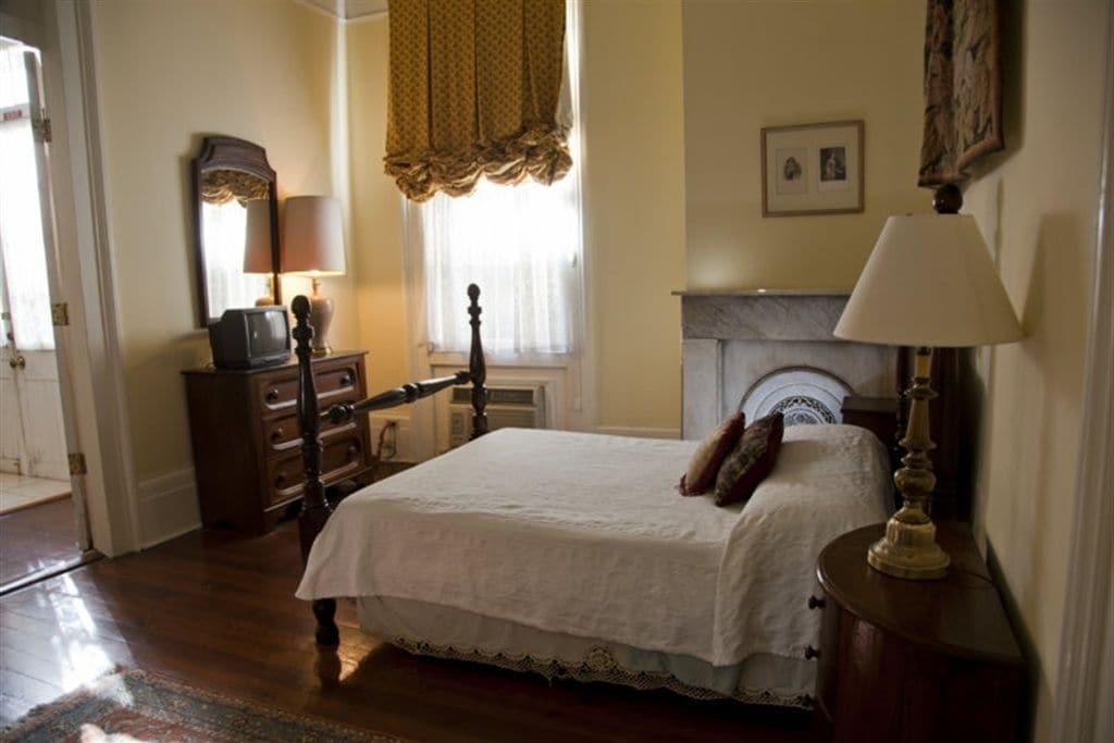 A bedroom with a bed, dresser, lamp, and fireplace.