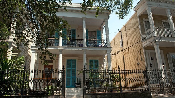 Um edifício de dois andares com varanda, colunas e grade de ferro forjado.