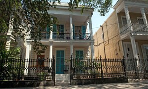 Un edificio de dos pisos con balcón, columnas y una cerca de hierro forjado.