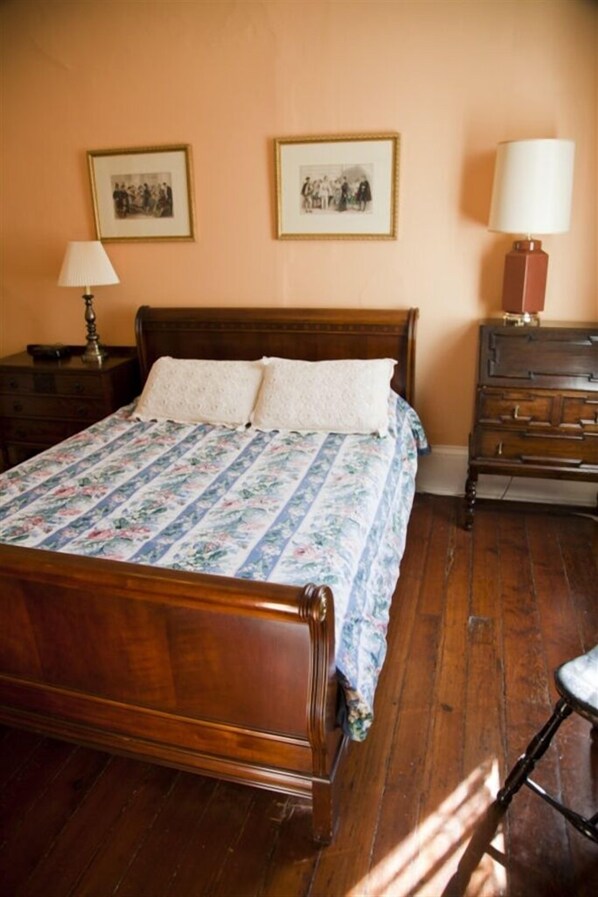 Un dormitorio con una cama de madera, una mesita de noche con lámpara, un aparador y dos cuadros en la pared.