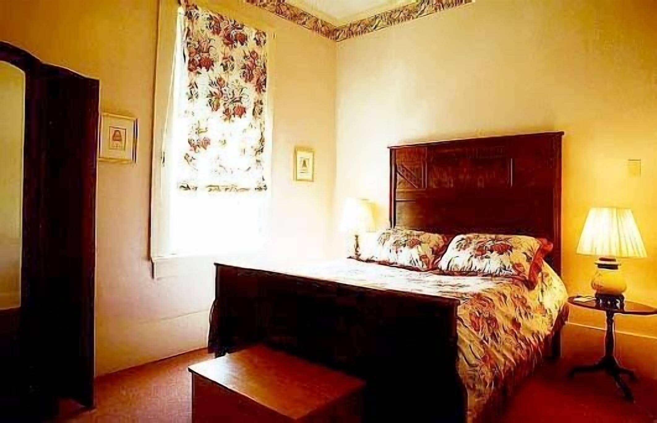 Une chambre à coucher avec un lit, une table de chevet, une lampe et une fenêtre avec des rideaux.
