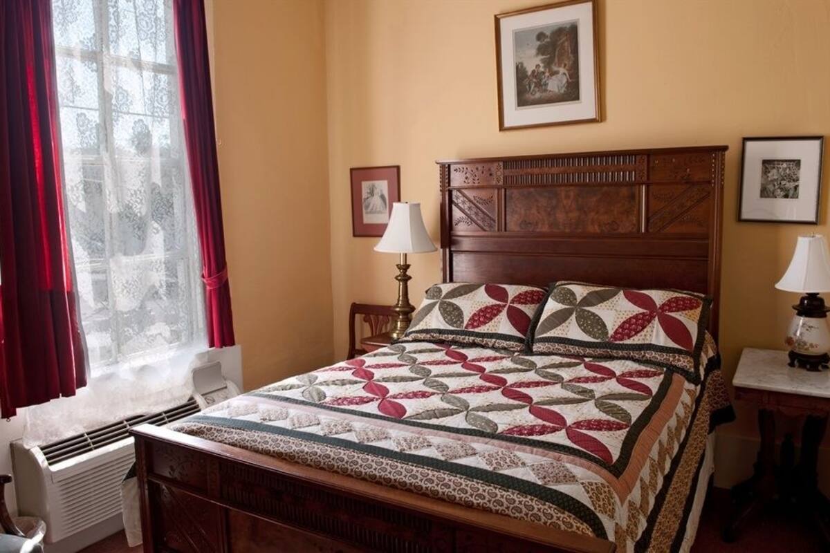 A bedroom with a wooden bed, two bedside tables with lamps, a radiator, and a window with curtains.