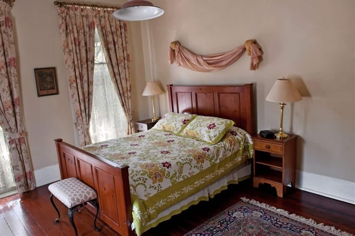 A bedroom with a wooden bed, two bedside tables with lamps, a bench, and a patterned rug.