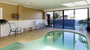 A swimming pool with a glass enclosure, a patio area with chairs, and a sliding glass door leading to an outdoor space. - Central City Motor Inn (Bakery Hill)