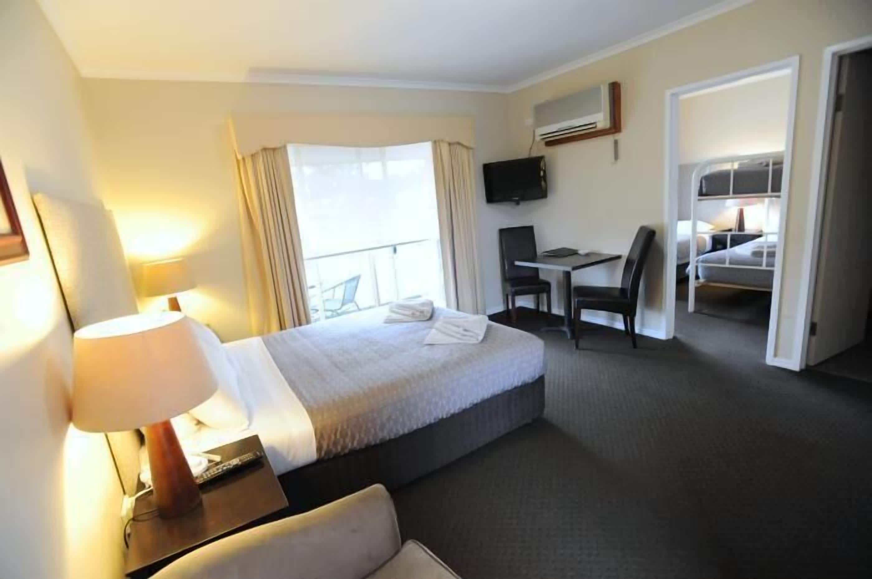 A hotel room with a bed, a desk, a chair, a TV, and a balcony.