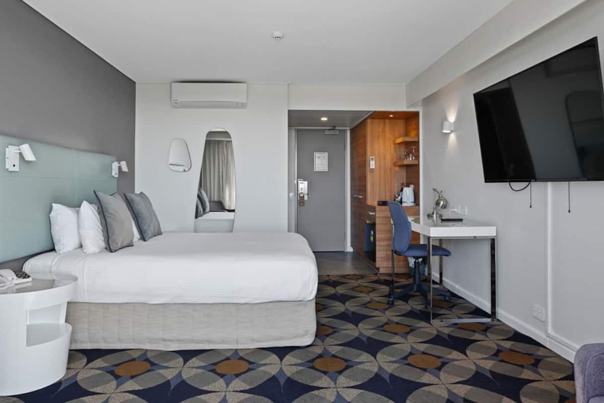 A hotel room with a bed, a desk, a chair, a TV, and a bathroom.