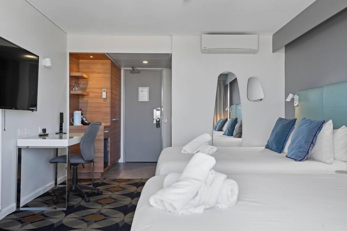 A hotel room with a bed, a desk, a chair, a television, and a bathroom visible through an open door.