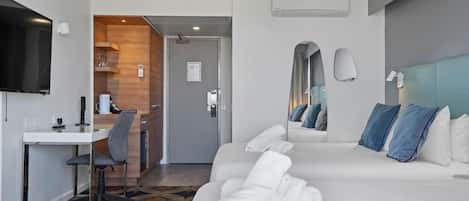 A hotel room with a bed, a desk, a chair, a television, and a bathroom visible through an open door.