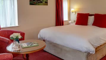Una habitación de hotel con una cama grande, cortinas rojas, una mesita con un jarrón de flores y un cuadro en la pared.