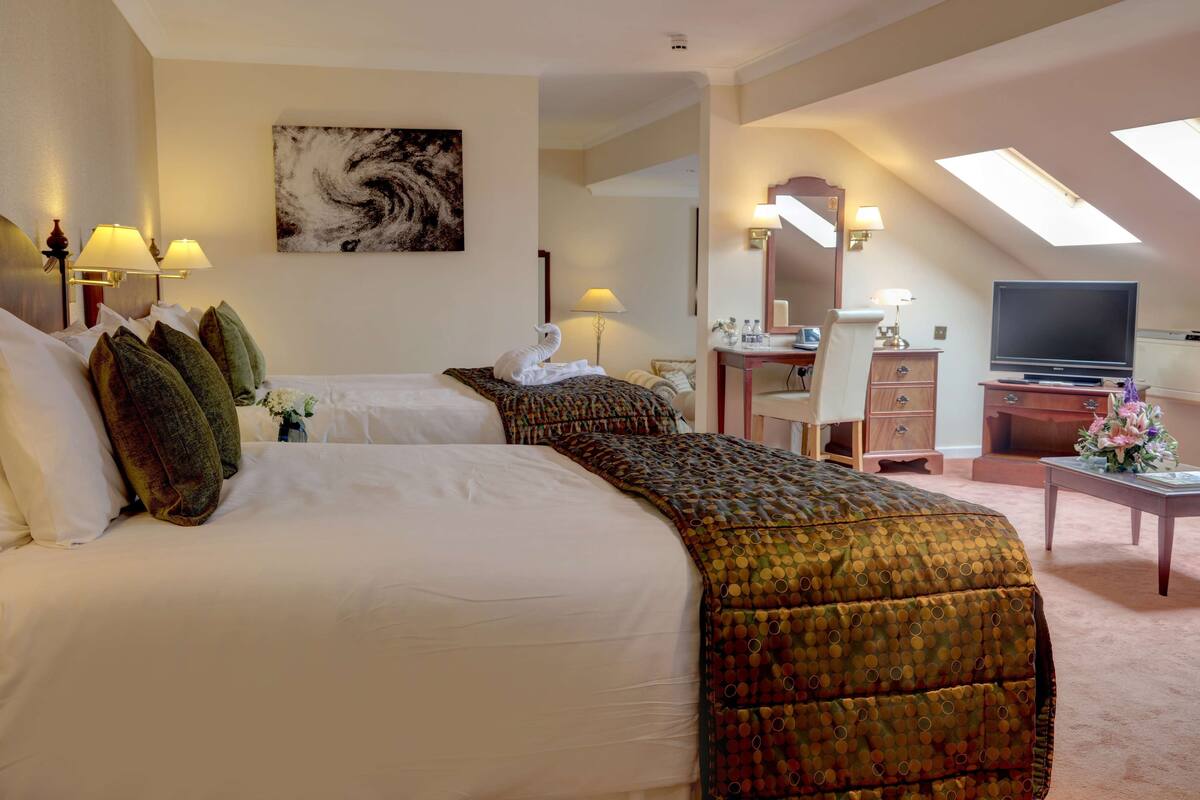 A hotel room with two beds, a desk, a TV, and a skylight.