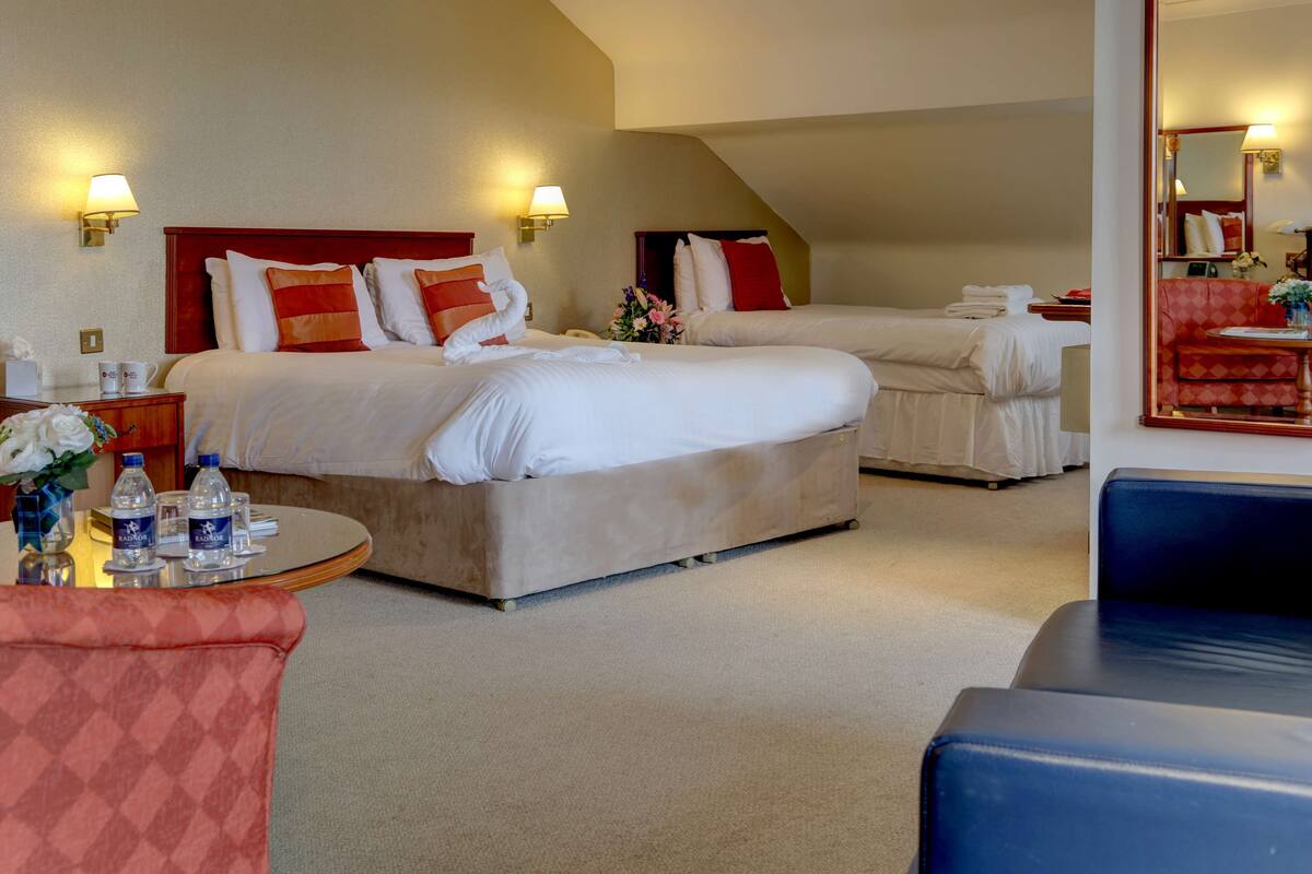 A hotel room with two beds, a round table with water bottles, a red armchair, and a blue couch.