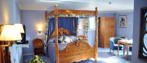 A four-poster bed with a canopy, a wooden desk, a chair, and a cabinet in a room with light blue walls.