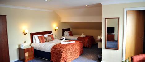 A hotel room with two beds, a small table with a vase of flowers, a mirror, and a wooden wardrobe.