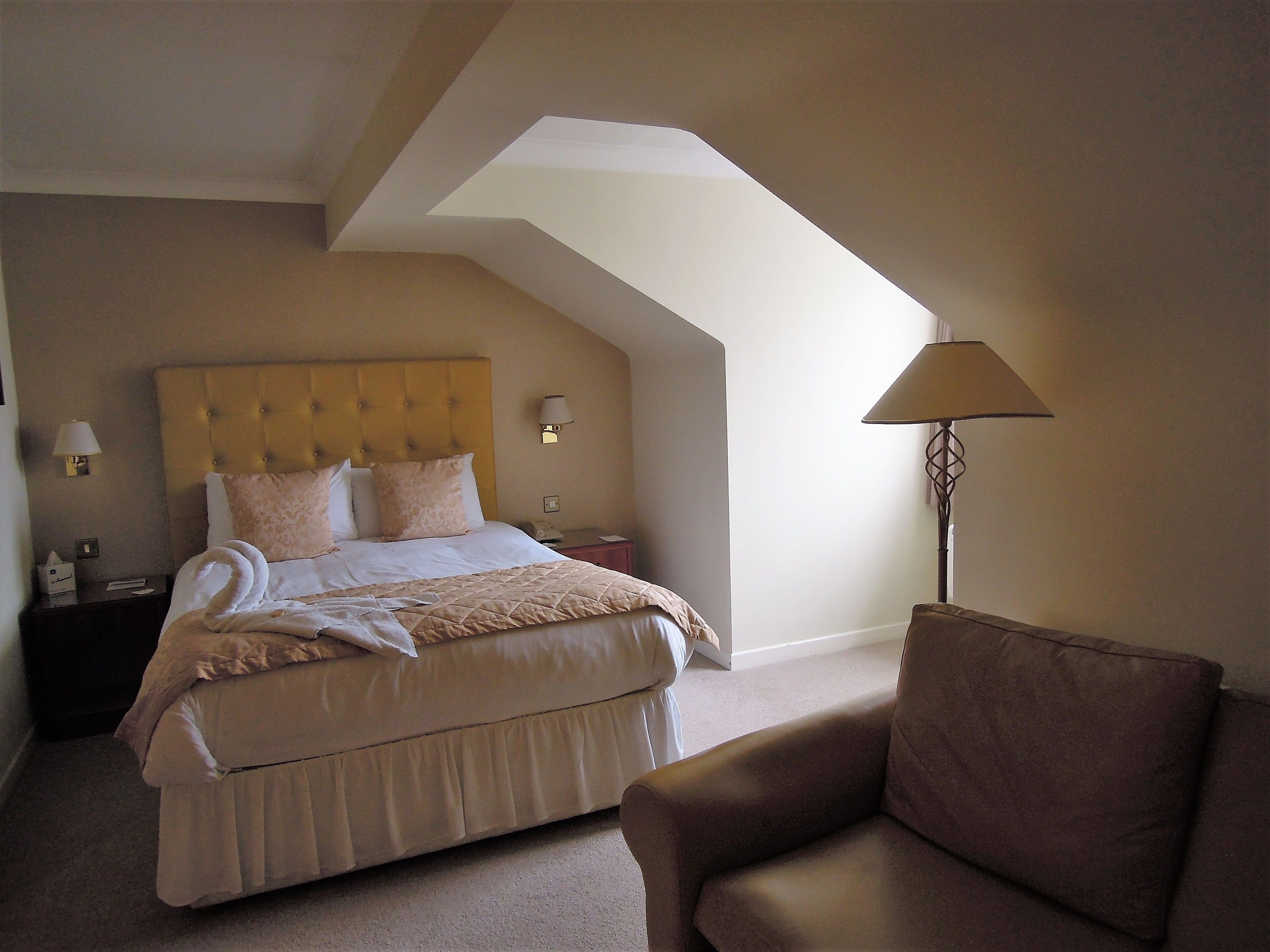 A hotel room with a large bed, a nightstand, a lamp, and a chair.