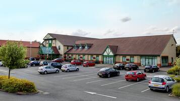 A parking lot with multiple cars parked in front of a building with a green and white facade.