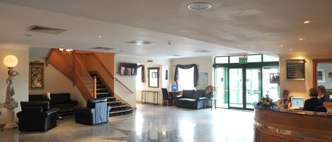 Eine Lobby mit Treppe, Sitzgelegenheiten, Empfangstresen und großen Fenstern.