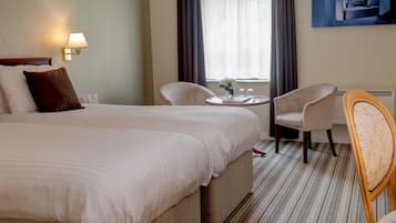 Ein Hotelzimmer mit einem großen Bett, zwei Stühlen, einem kleinen Tisch und einem Fenster mit Vorhängen.
