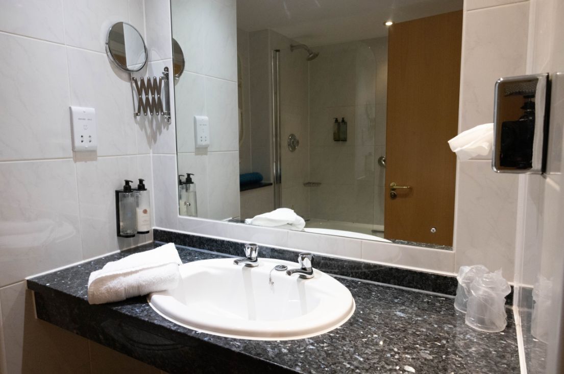 Un baño con lavamanos, espejo, toalla y ducha.