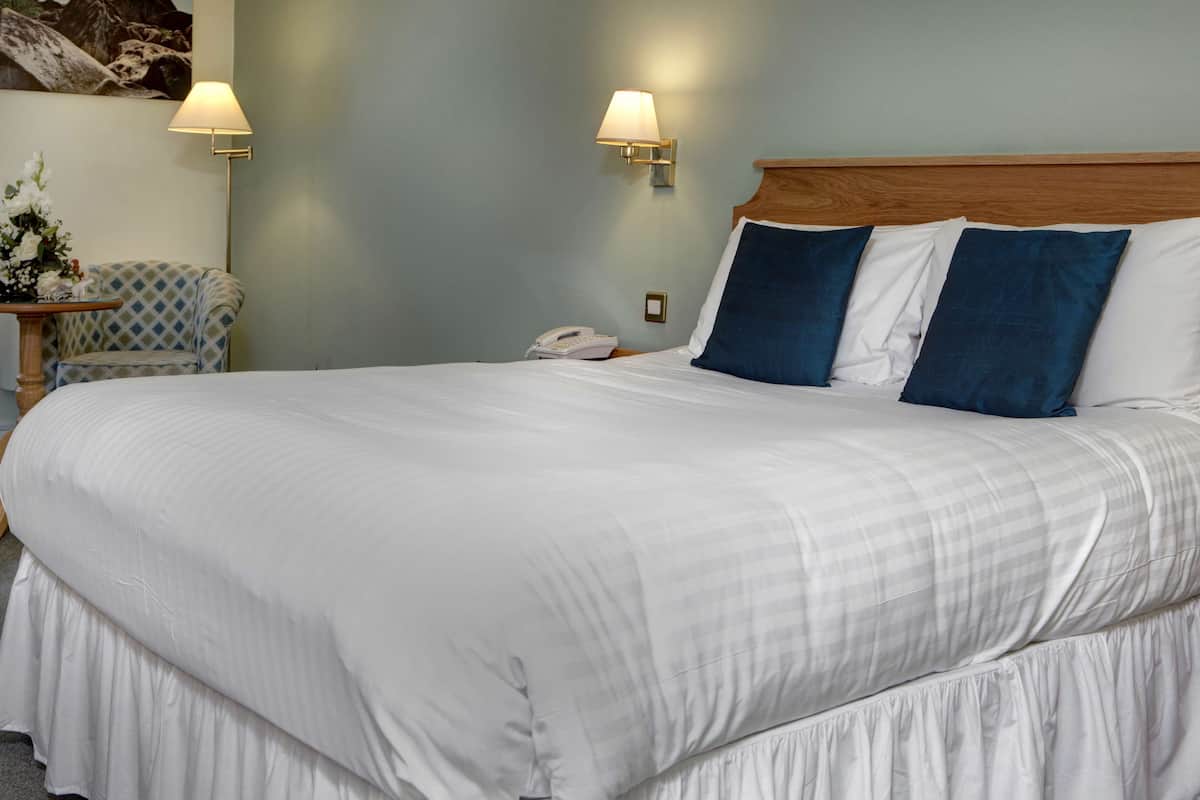 A neatly made bed with white and blue pillows, a bedside phone, and two wall-mounted lamps.