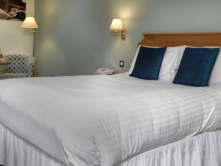 A neatly made bed with white and blue pillows, a bedside phone, and two wall-mounted lamps.