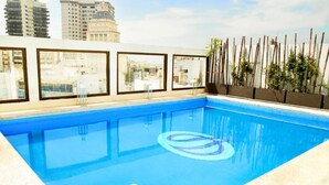 Una piscina en la azotea con agua cristalina y azul, rodeada de grandes ventanales que ofrecen vistas de la ciudad.