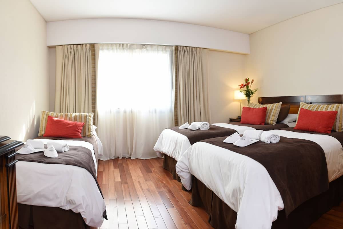 Una habitación de hotel con dos camas, piso de madera y ventana con cortinas.