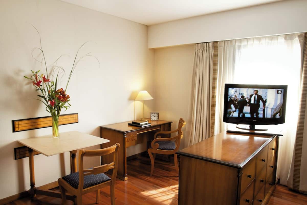 Habitación de hotel con un escritorio de madera, una silla, un televisor y un florero con flores.