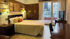 Une chambre d’hôtel avec un lit, des lampes de chevet, un bureau avec une télévision et une vue sur la ville par une grande fenêtre.