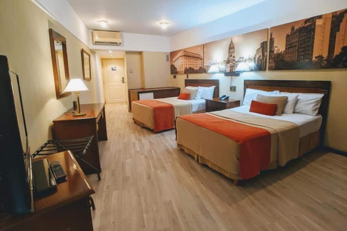 A hotel room with two beds, a desk, a chair, a lamp, and a painting on the wall.