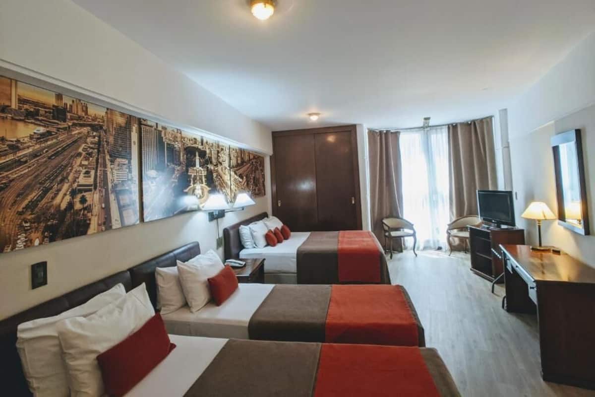 A hotel room with two beds, a desk, a television, and a large cityscape painting on the wall.