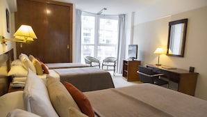 Une chambre d’hôtel avec deux lits, un bureau, une chaise, une télévision et une grande fenêtre avec des rideaux.