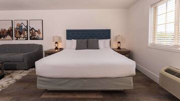 A bedroom with a large bed, two bedside tables with lamps, a grey sofa, and a rug.