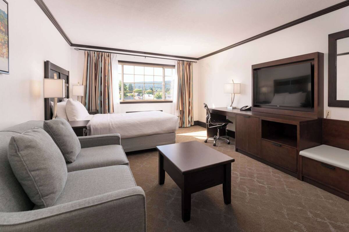 A hotel room with a bed, a sofa, a desk with a chair, a TV, and a bench.