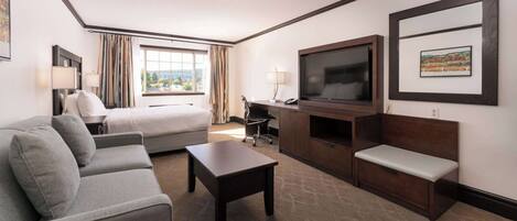 A hotel room with a bed, a sofa, a desk with a chair, a TV, and a bench.