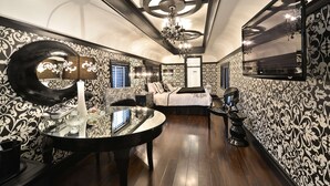 A luxurious bedroom with a large mirror, ornate wallpaper, a chandelier, and a modern bed. - Prestige Rocky Mountain Resort Cranbrook, WorldHotels Crafted (Cranbrook)