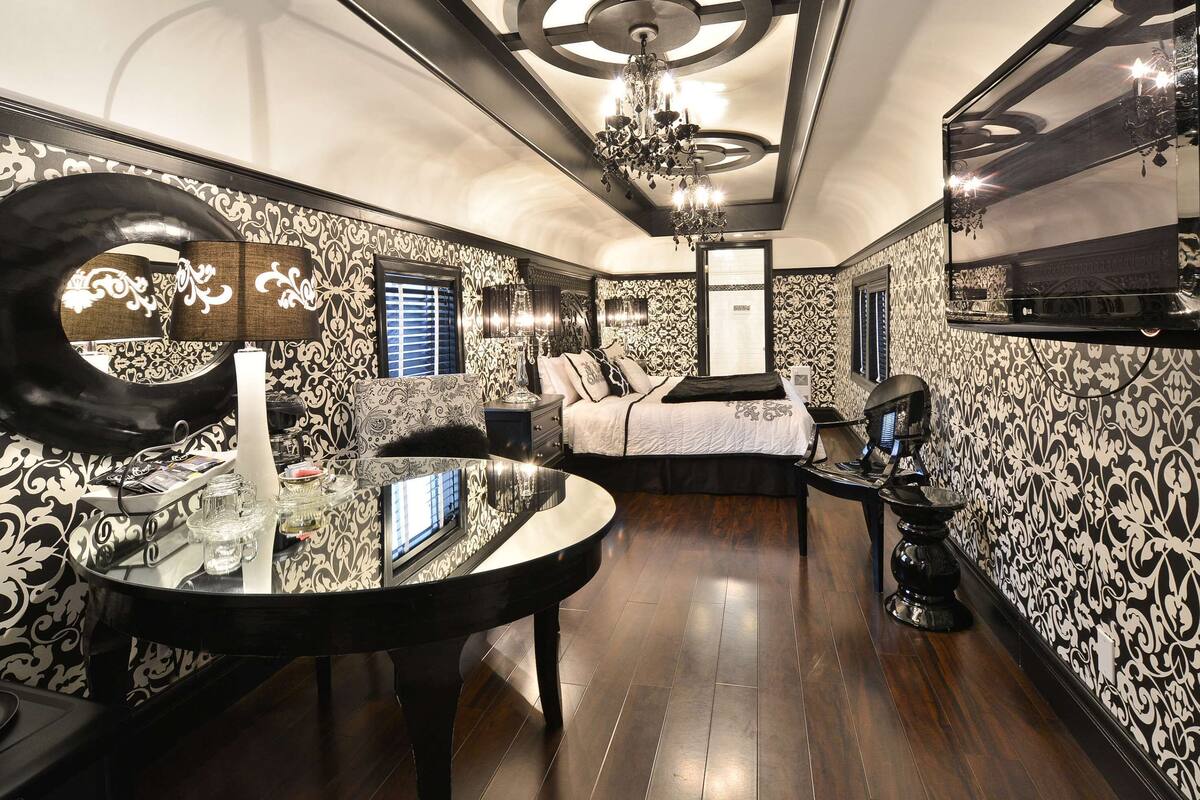 A luxurious bedroom with a large mirror, ornate wallpaper, a chandelier, and a modern bed.