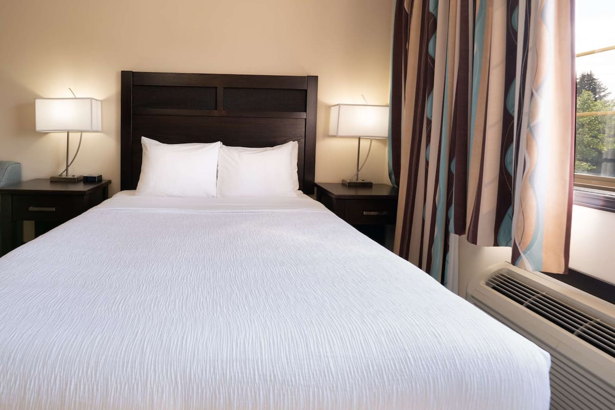 A hotel room with a large bed, two bedside tables with lamps, a chair, and a window with curtains.