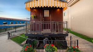 A train car converted into a stationary building with a balcony, a door, and a small window. - Prestige Rocky Mountain Resort Cranbrook, WorldHotels Crafted (Cranbrook)