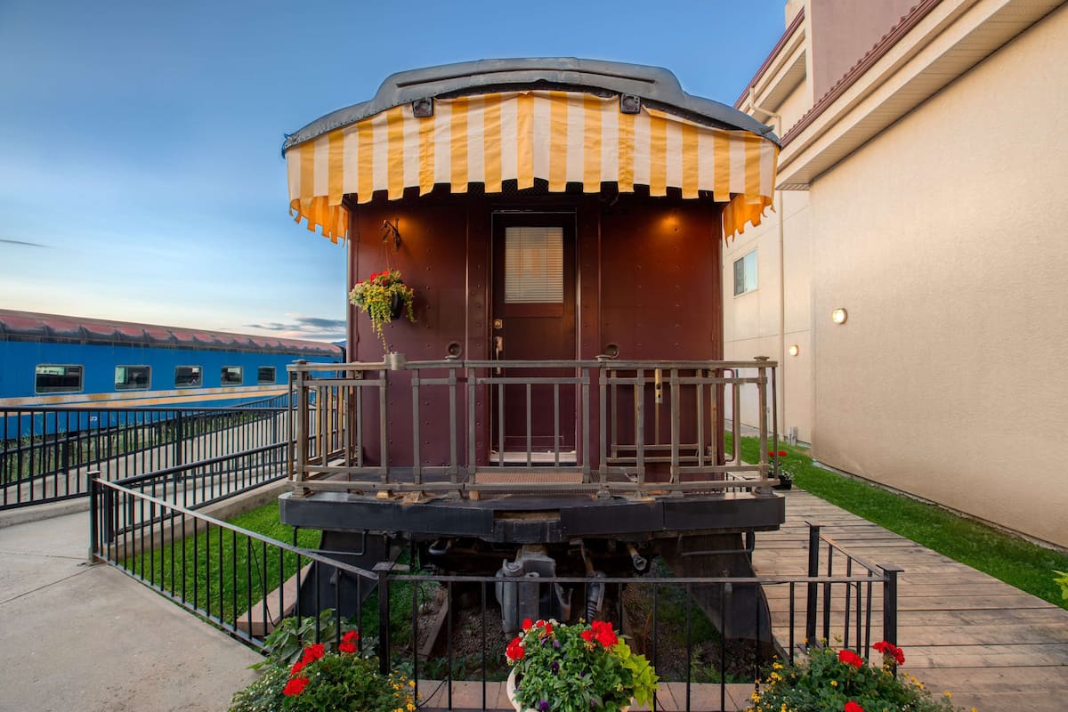 A train car converted into a stationary building with a balcony, a door, and a small window.