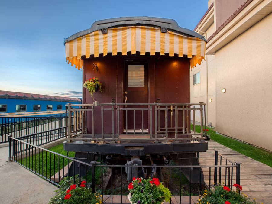 A train car converted into a stationary building with a balcony, a door, and a small window.