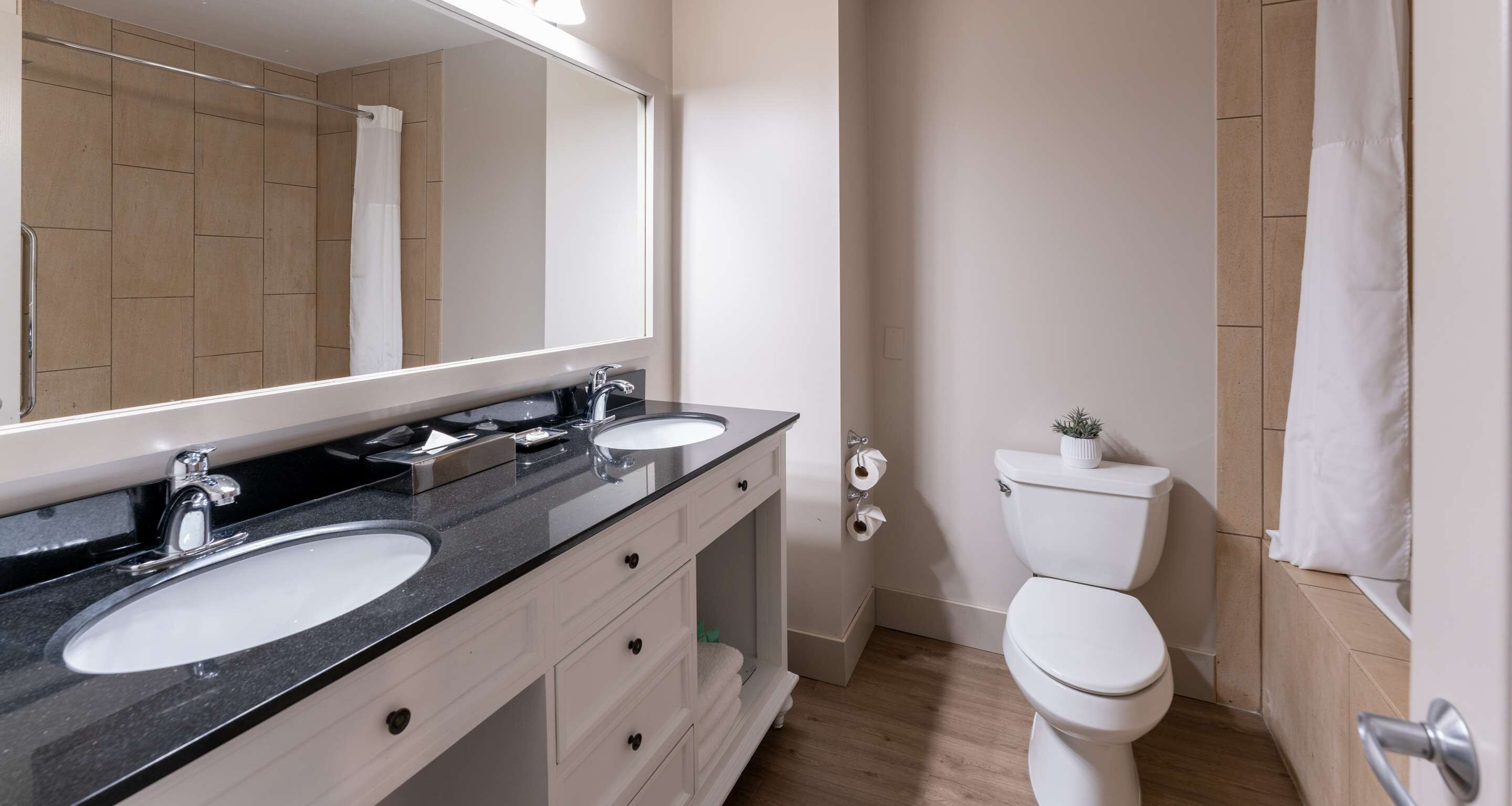 Une salle de bain moderne avec deux lavabos, un grand miroir et des toilettes.
