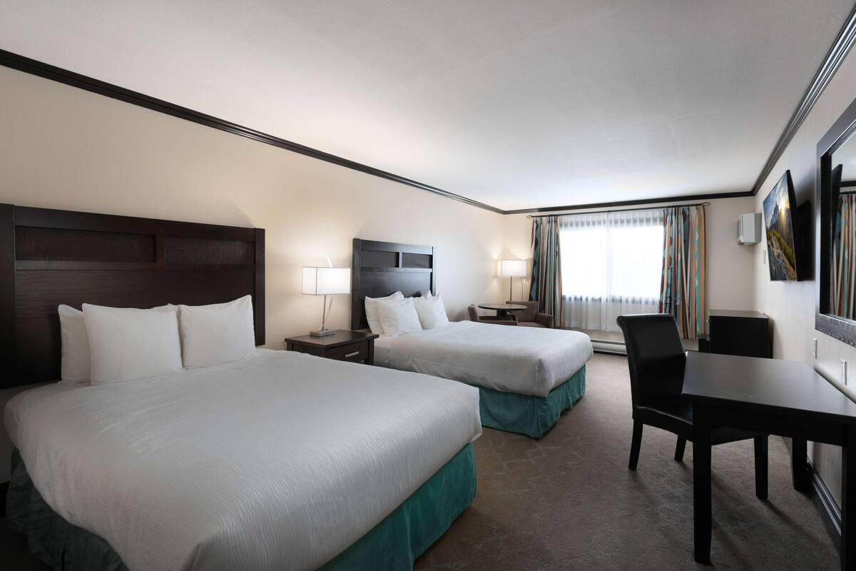 A hotel room with two beds, a desk, and a chair.