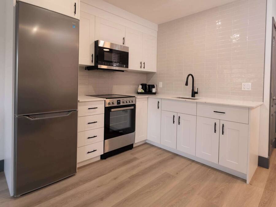 A modern kitchen with white cabinets, a stainless steel refrigerator, a microwave, an oven, and a black faucet.