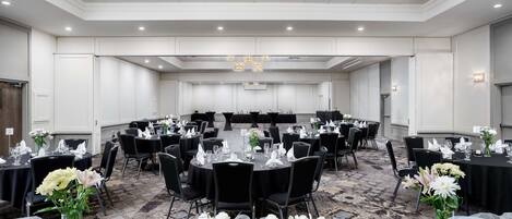 Un salón de banquetes con mesas redondas preparadas para eventos, con manteles negros, servilletas blancas y centros de mesa florales.