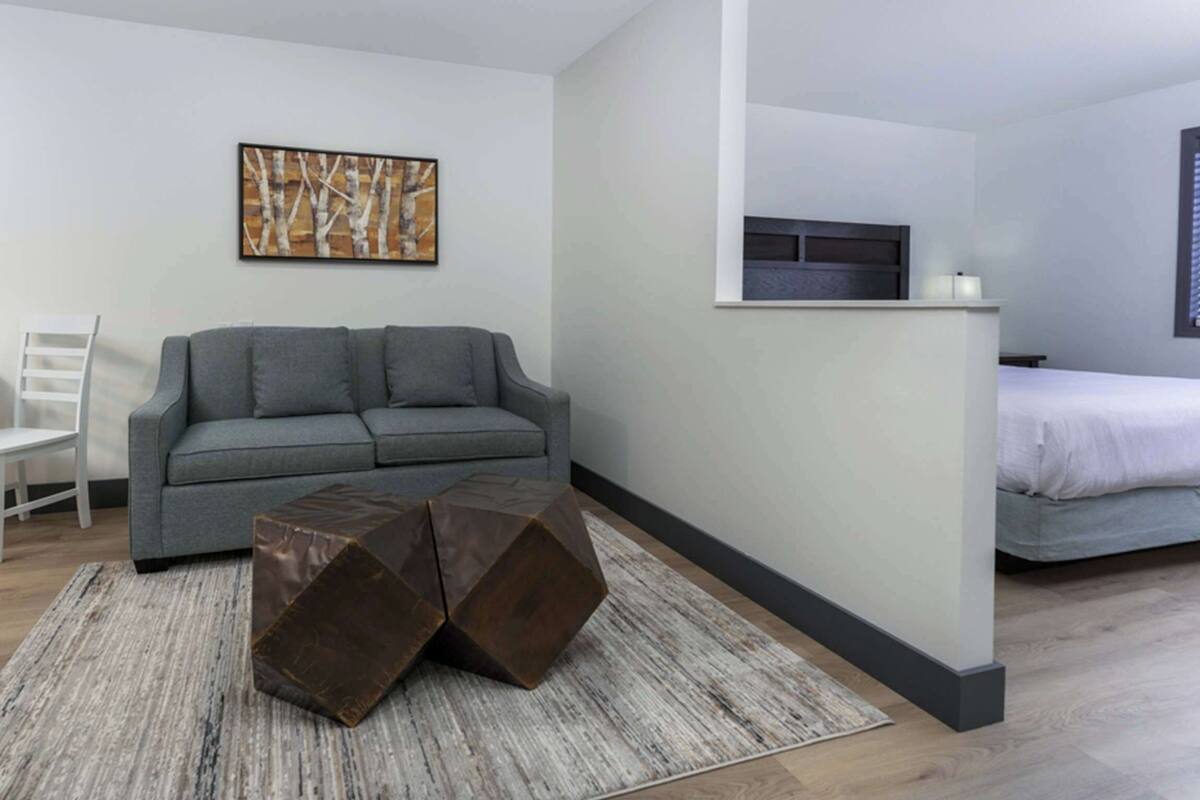 A modern living room with a grey sofa, a white chair, a coffee table, and a painting on the wall.